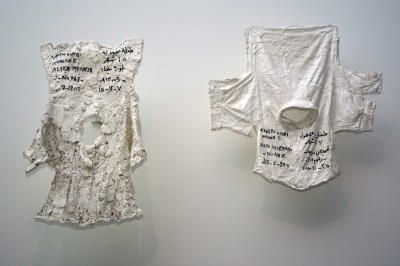 In Issam Kourbaj’s “Lost,” children’s clothing acts as a gravestone for the child who didn’t make it across the Aegean Sea. Descriptions and dates of death are written in both Arabic and Greek: “Unknown girl, 15 months old, white blouse, No. 963, 7-12-2015” and “Unknown boy, 17 months old, checked shirt, No. 487, 25-11-2015.”