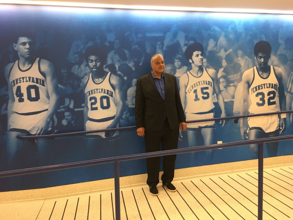 Tony Price, posing next to an old photo of himself, in the newly decorated Tse Center Atrium.