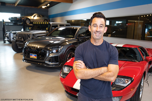 Photo of Matthew Pohlson standing in front of cars to be auctioned as fundraising prizes 