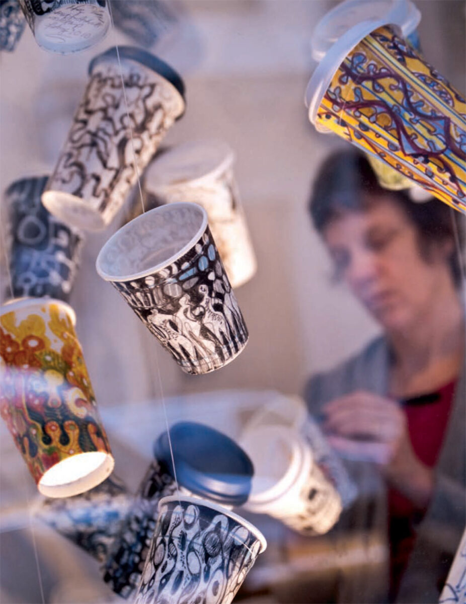 Photograph of hanging decorated cups with artist Gwyneth Leech in background